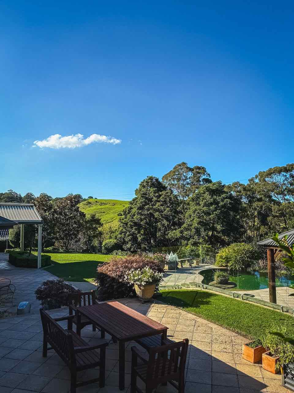 Paved terrace and timber outdoor setting overlooking lawn, pool fencing and green escarpment hills